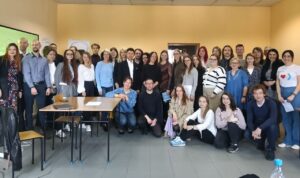 Zdjęcie przedstawia grupę 40 osób stojących w sali uczelnianej na tle źółtej ściany