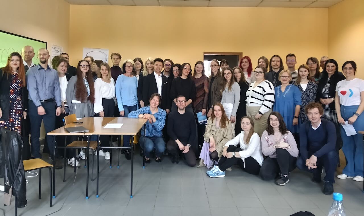 Zdjęcie przedstawia grupę 40 osób stojących w sali uczelnianej na tle źółtej ściany