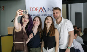 Cztery młode osoby fotografujące się na tle rollupu z napisem TopMinds